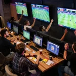Engaged sports bettors excitedly placing wagers on Da88 at a modern sports bar with multiple screens
